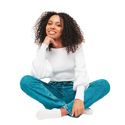 A smiling woman in a white sweater and jeans sitting cross-legged against a plain background