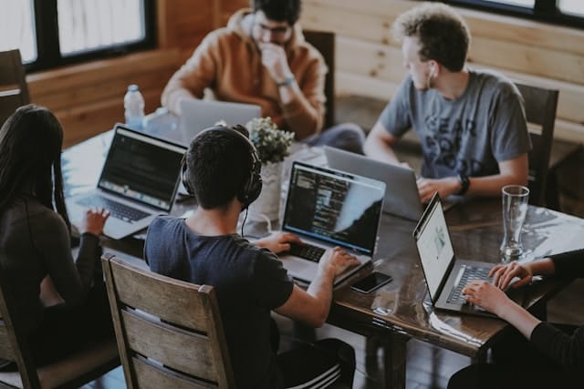 A team of developers and designers working together on laptops around a shared wooden table